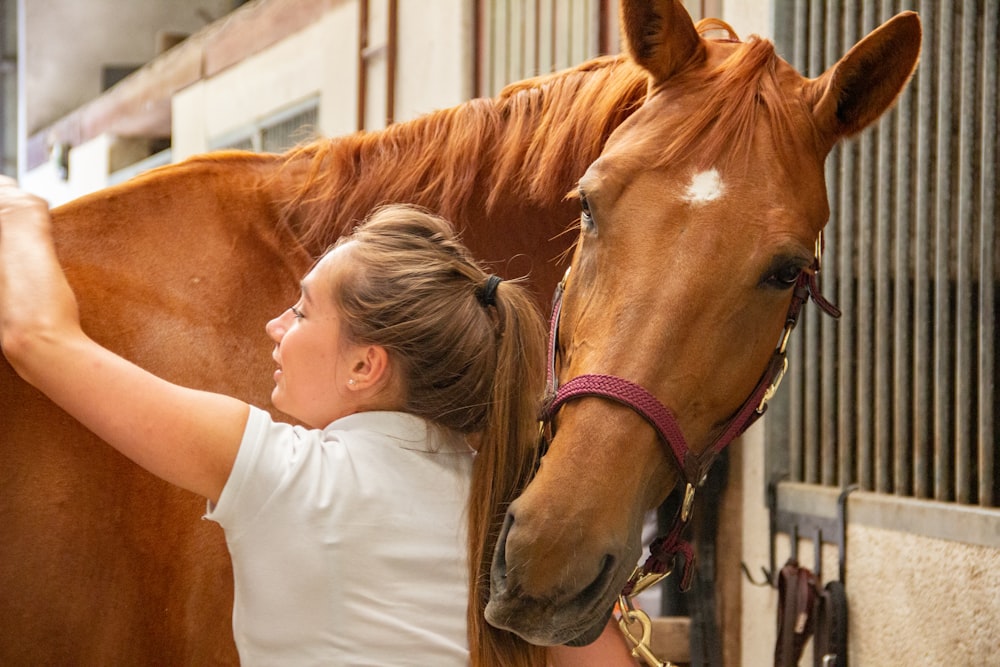 woman in white crew neck t-shirt standing beside brown horse during daytime