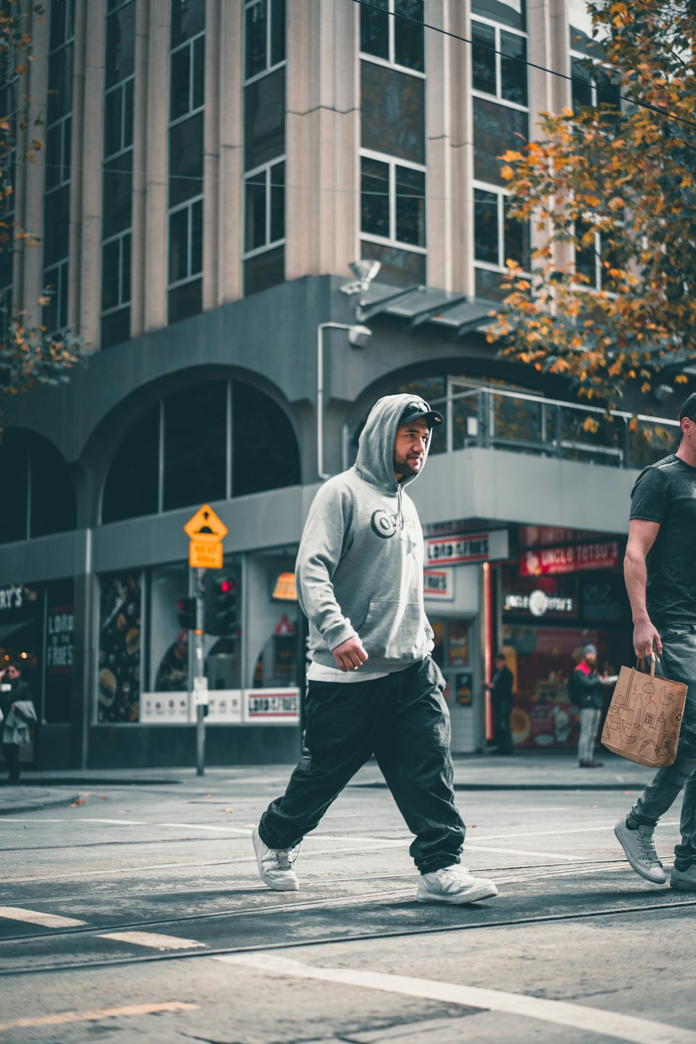 man in white hoodie and black pants walking on sidewalk during daytime