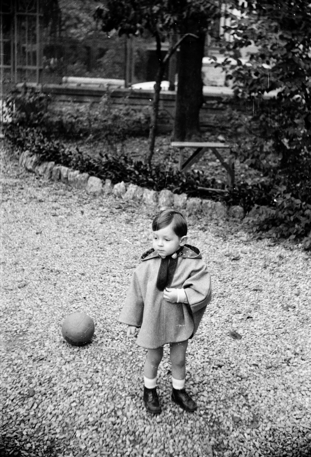 grayscale photo of girl in green coat standing on grass field