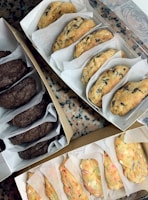 Three open boxes containing different varieties of cookies, such as chocolate chip, double chocolate, and funfetti, placed on a speckled countertop.