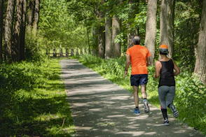 man in orange t-shirt and gray pants with blue shoes walking on pathway