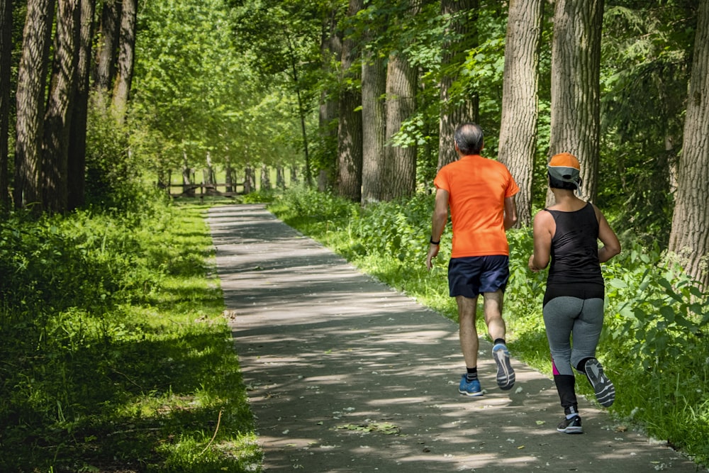 man in orange t-shirt and gray pants with blue shoes walking on pathway