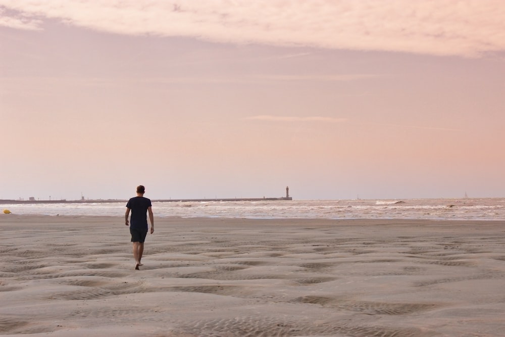 man in black shirt walking on beach during daytime