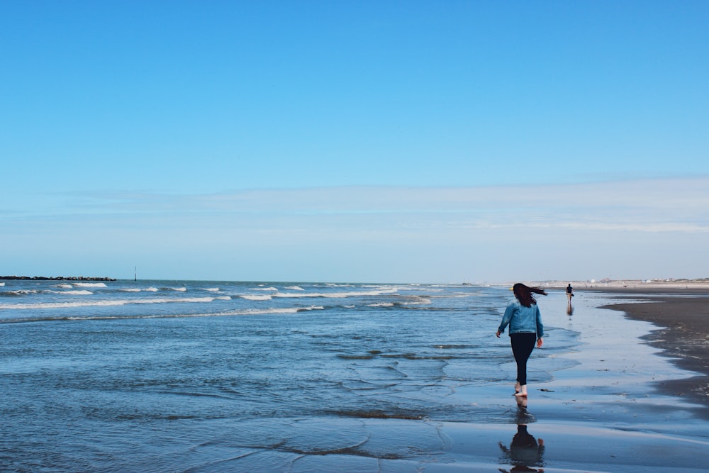 man in black jacket and blue denim jeans walking on beach during daytime