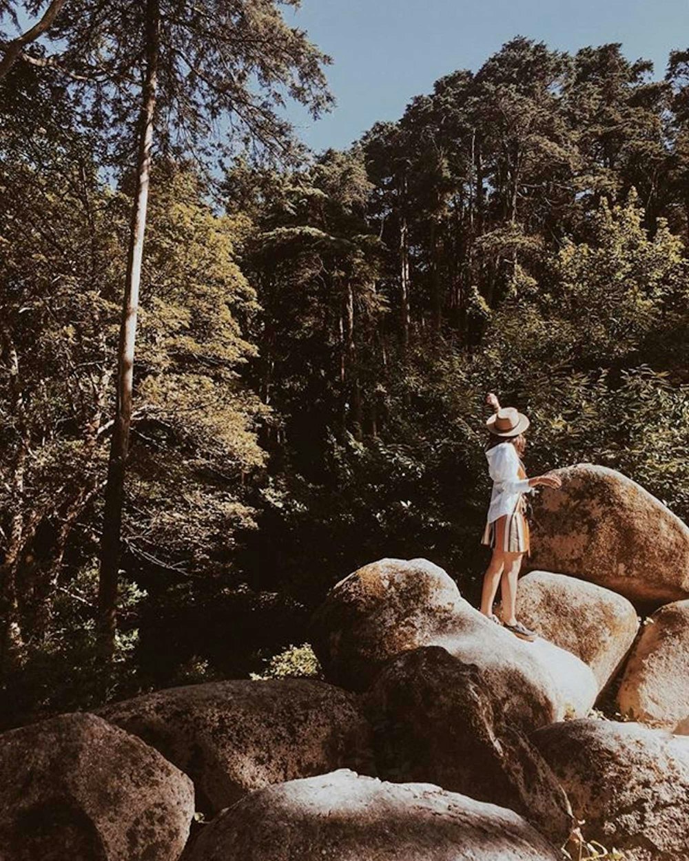 man in white t-shirt and blue denim shorts standing on brown rock during daytime