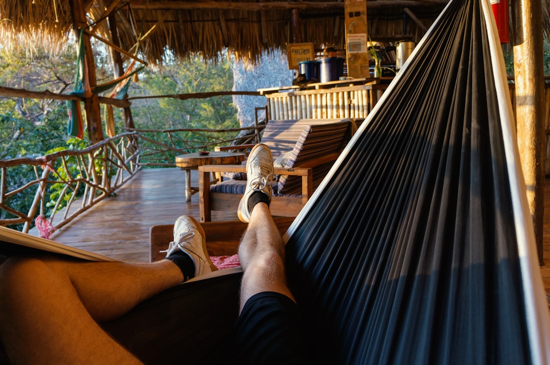 person in black shorts sitting on brown wooden bench, Guy with white shoes lounging in a HÄNG.COM Camping Hammock