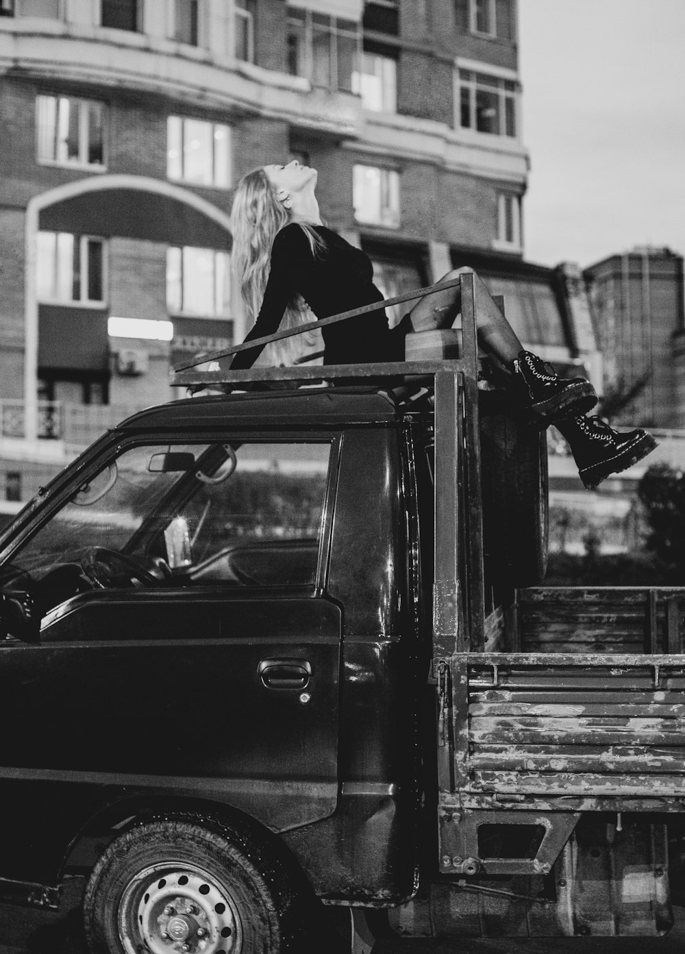 grayscale photo of woman in black jacket and white knit cap standing beside car