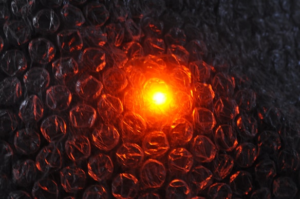 The image features a close-up view of bubble wrap illuminated from behind by a glowing orange light, creating a contrast with the transparent plastic material.