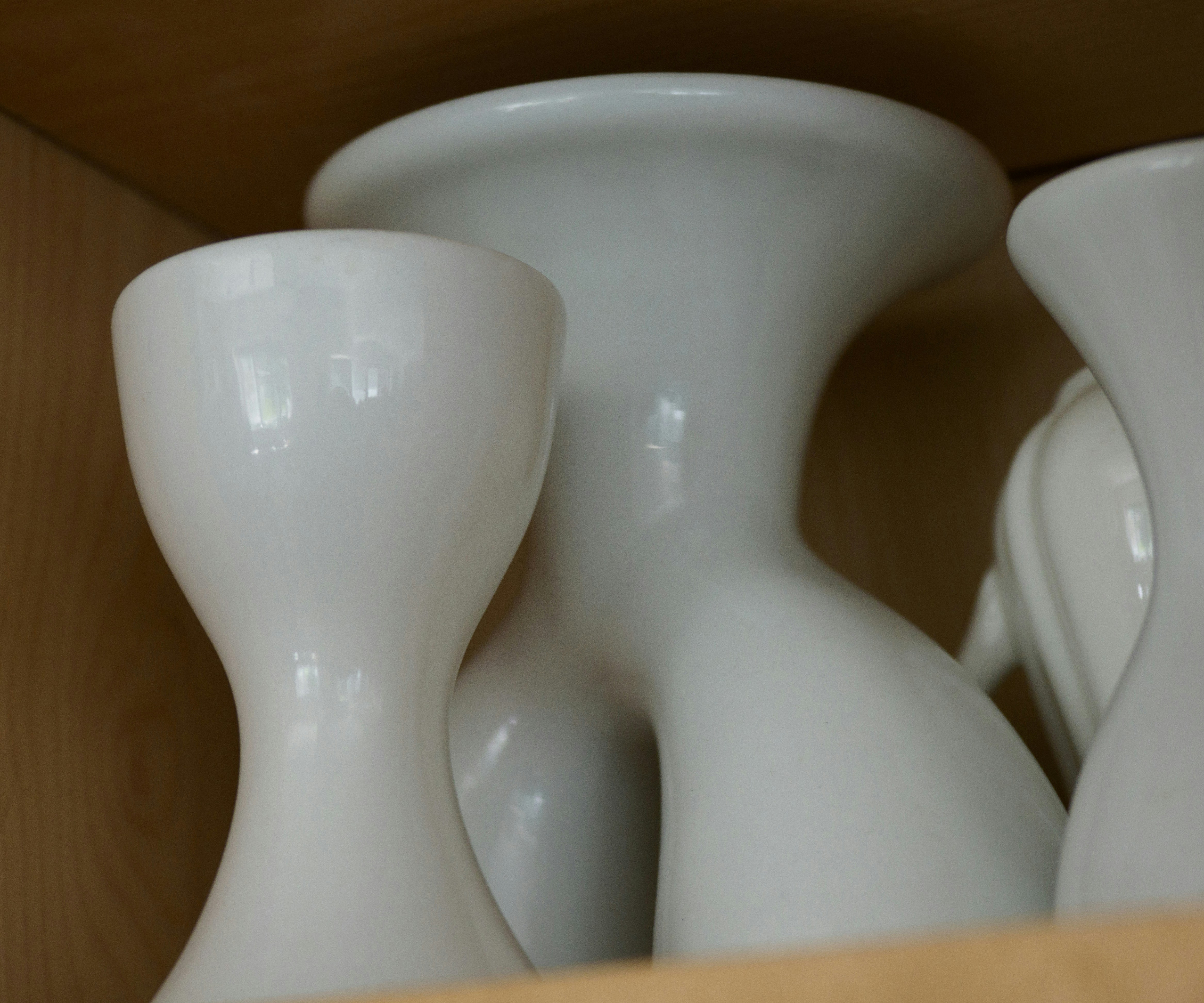 Set of three white ceramic plant pots of different sizes on light wood shelf