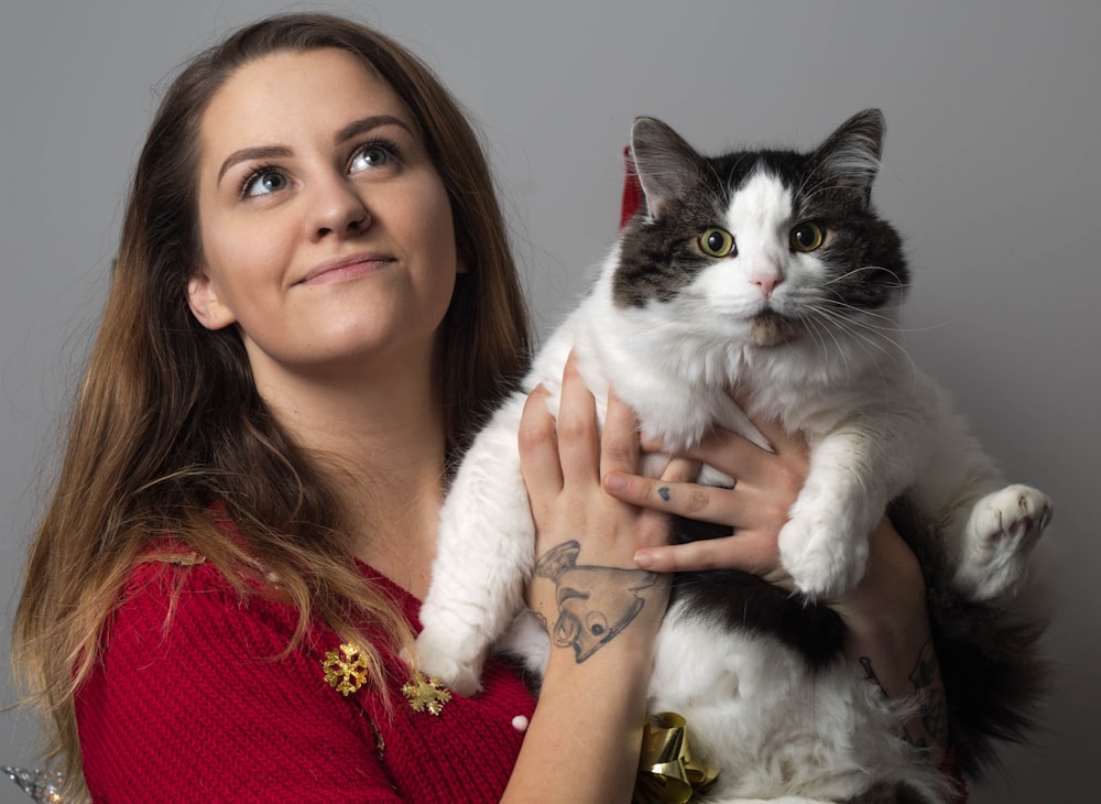 woman in red knit sweater holding white and black cat