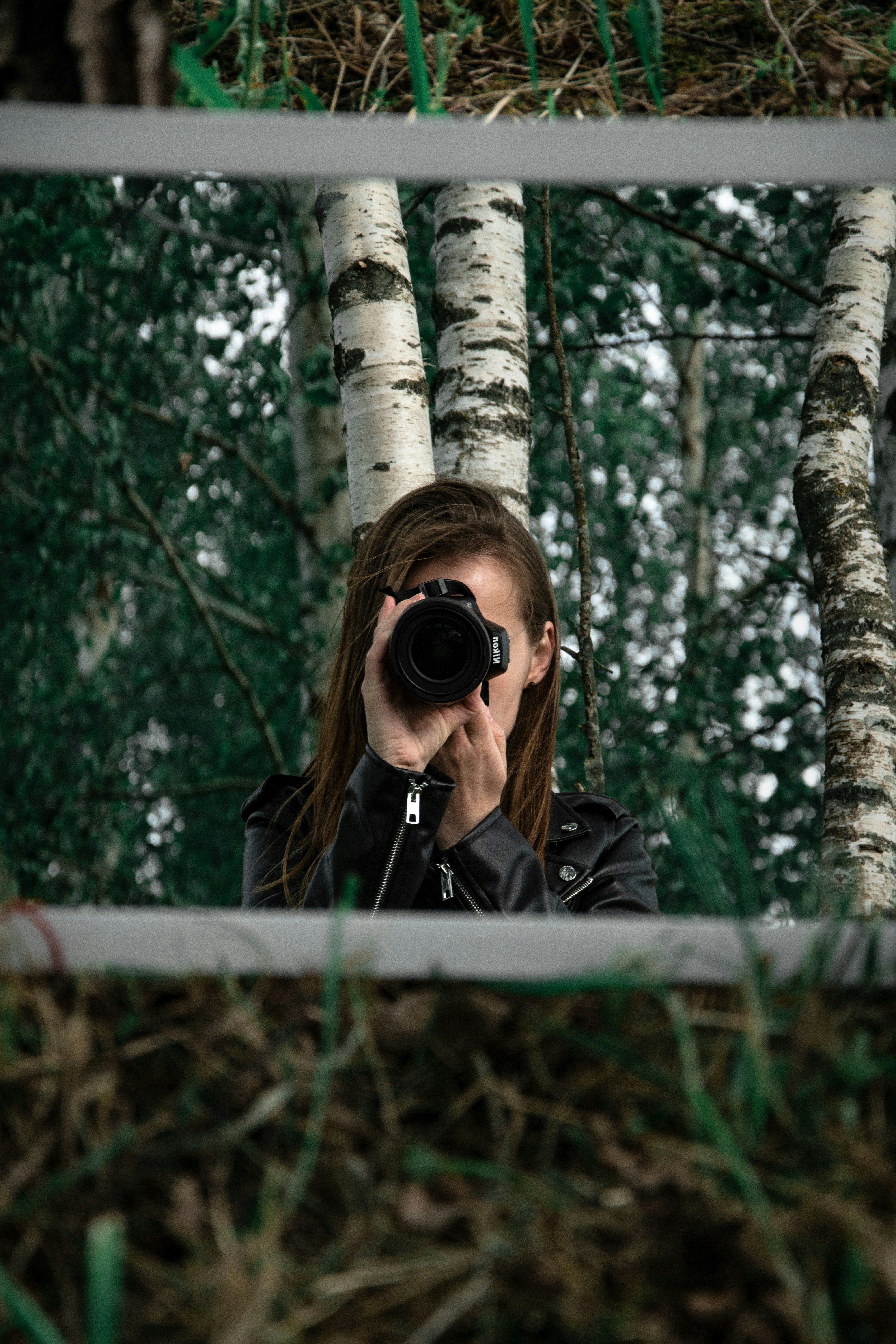 Donna in giacca di pelle nera che tiene la fotocamera DSLR nera