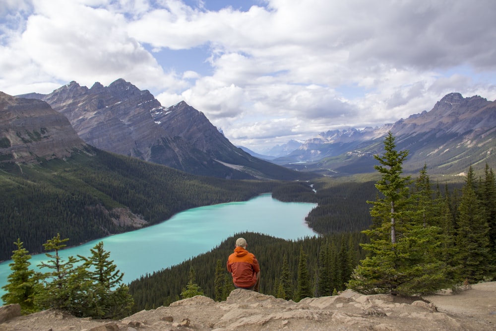 person in orange hoodie sitting on rock near lake during daytime