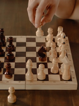 A child thoughtfully moving a chess piece on a wooden chessboard in a bright, cheerful classroom.