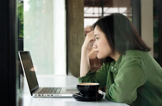 woman in green jacket sitting by the table using laptop