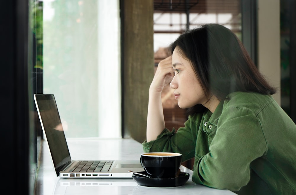 woman in green jacket sitting by the table using laptop