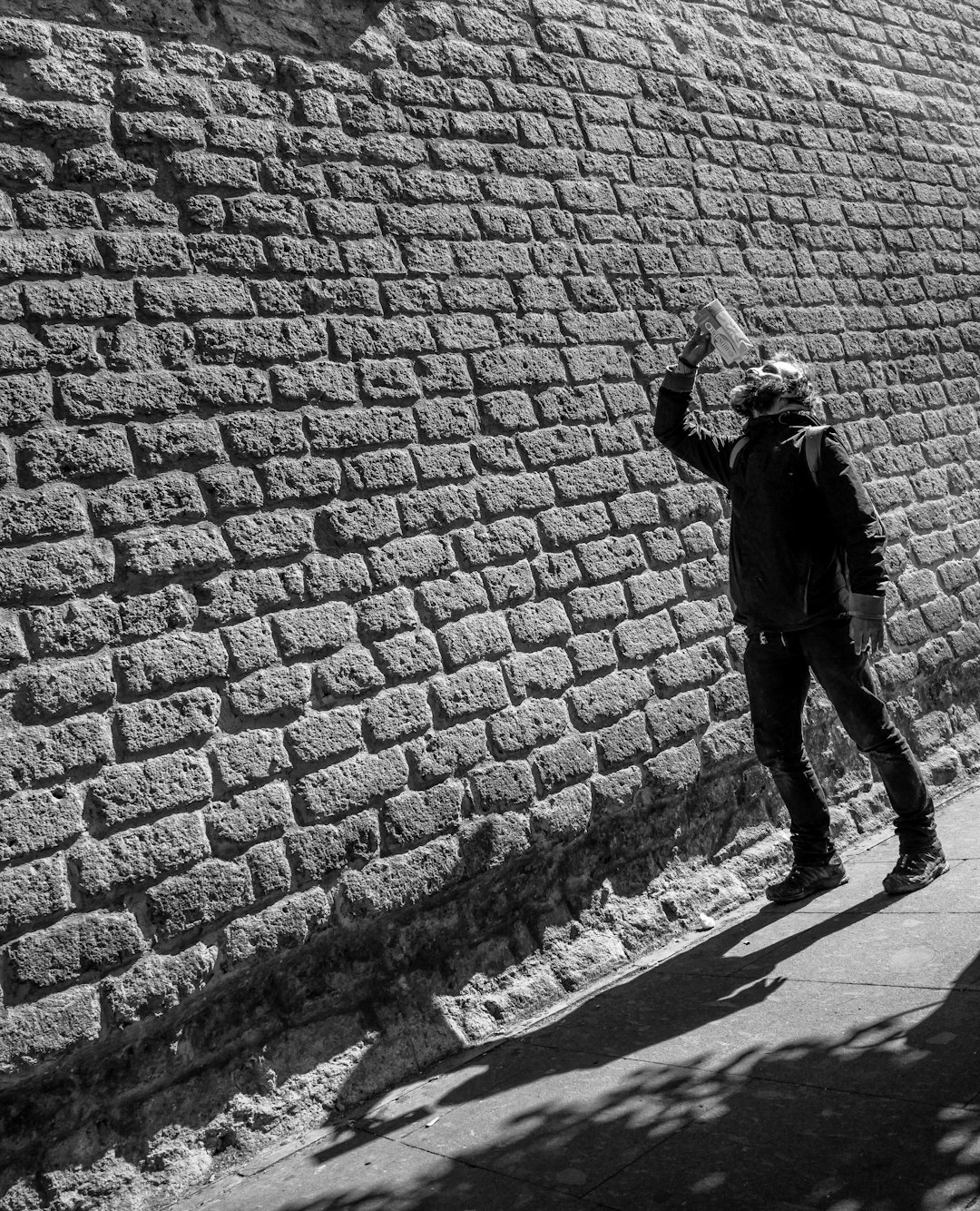 man in black jacket and pants standing on brick wall