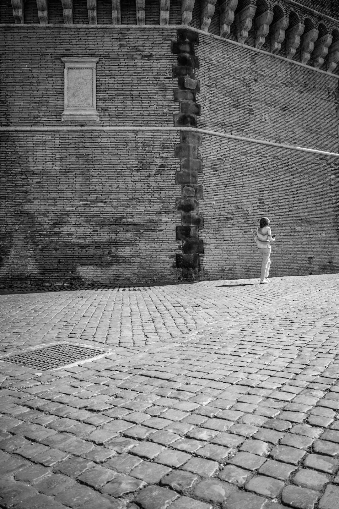 grayscale photo of woman walking on brick pavement