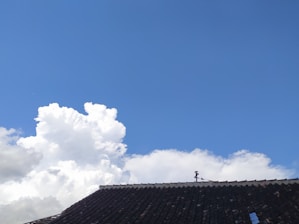 Photo of a skilled roofer installing shingles on a residential roof under clear skies.