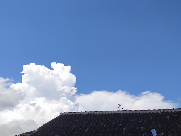 Photo of a skilled roofer installing shingles on a residential roof under clear skies.