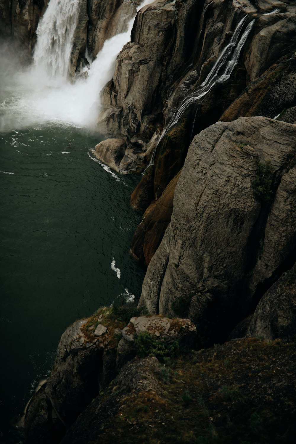 water falls between brown rocky mountain during daytime