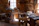 A traditional woodworking shop with a variety of tools and benches, lit by natural light streaming through windows. Tools such as saws, hammers, and chisels are organized on shelves and wooden benches, and a wooden floor is covered with wood shavings.