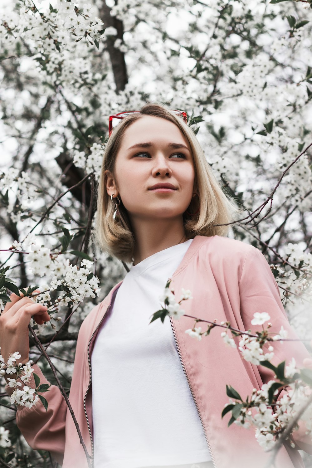 woman in pink long sleeve shirt standing near cherry blossom tree during daytime