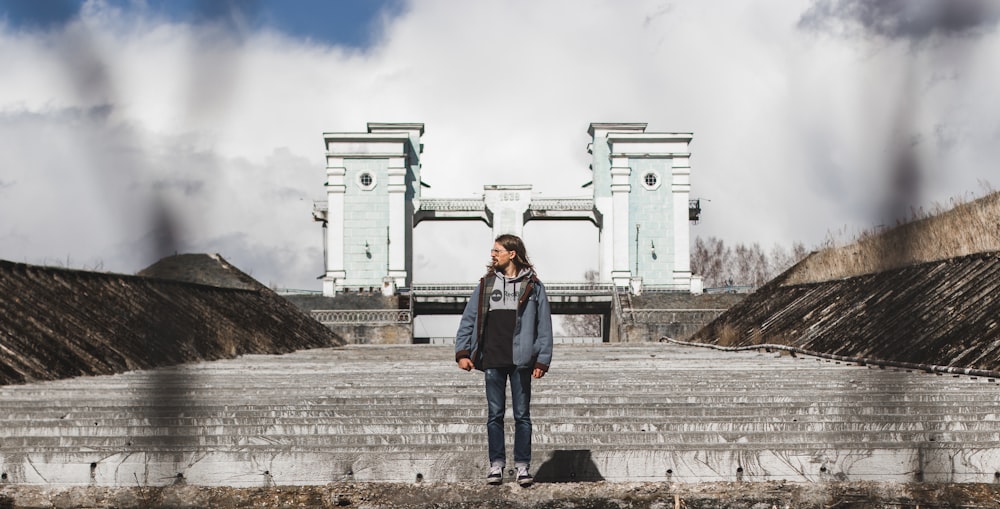 man in blue denim jacket standing near white concrete building during daytime