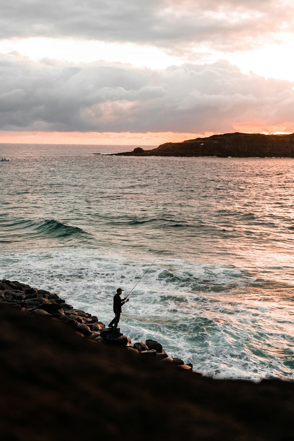 man in black jacket standing on rock near sea during daytime