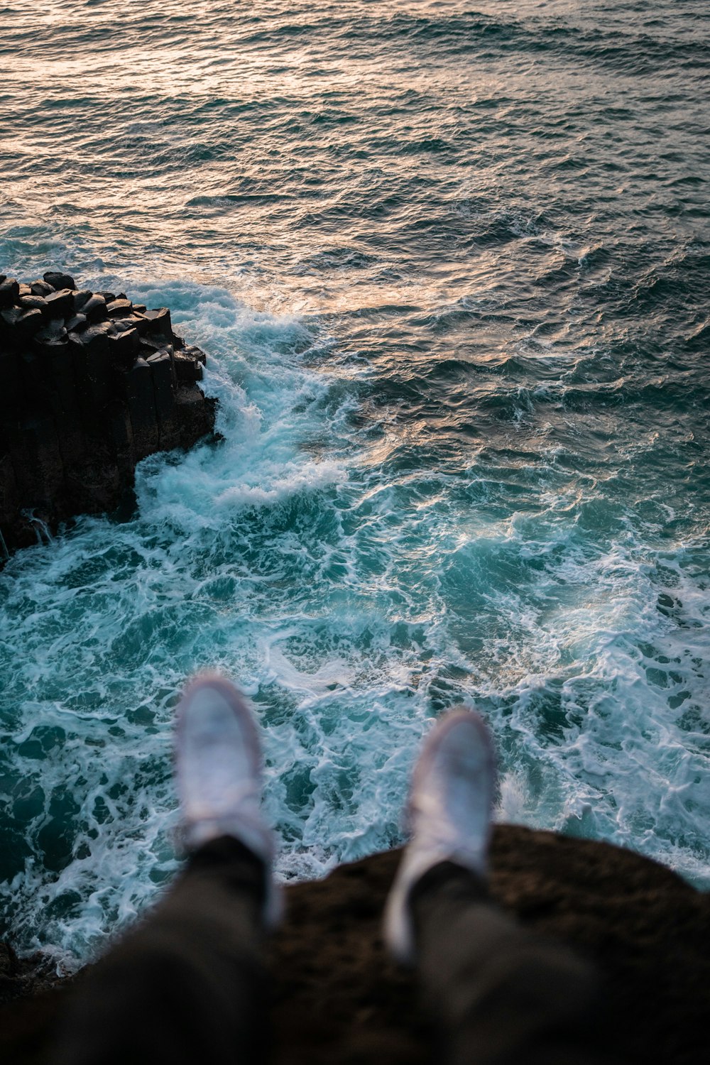 person in blue denim jeans standing on rock formation in front of body of water during