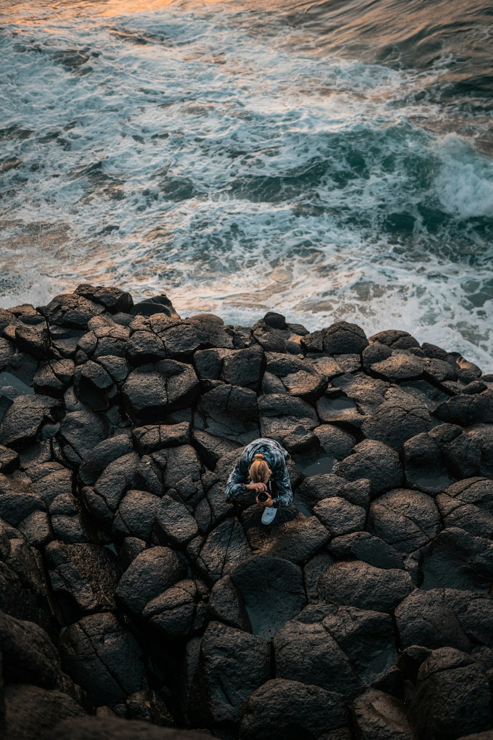 pessoa em jaqueta azul e calças pretas em pé na costa rochosa durante o dia