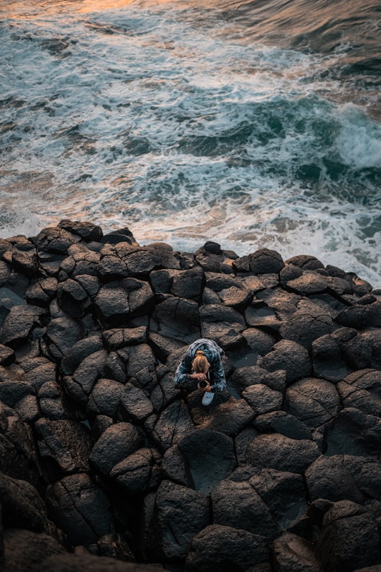 person in blue jacket and black pants standing on rocky shore during daytime in Fingal Head Australia