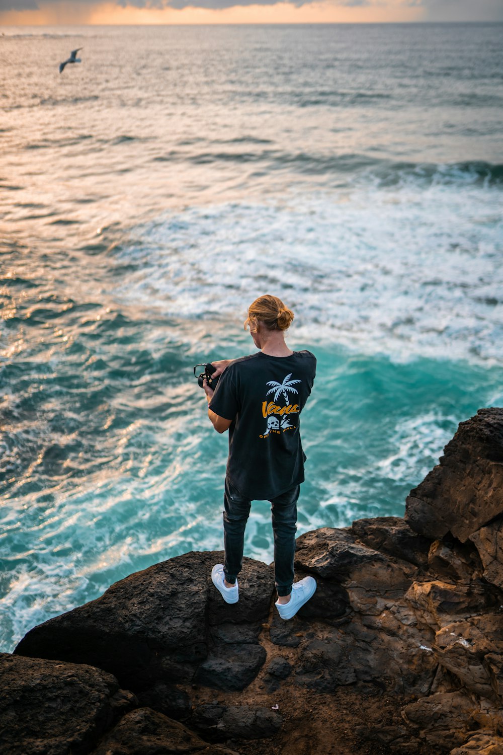 昼間、海の近くの岩の上に立つ青いクルーネックTシャツを着た少年
