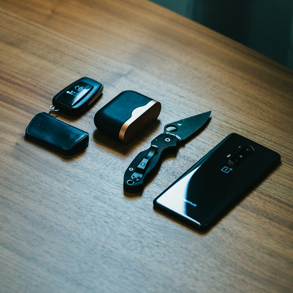 black and silver pocket knife beside black iphone 4 on brown wooden table