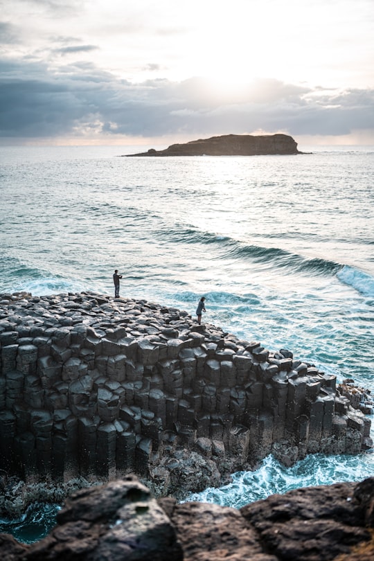 person standing on rock formation near sea during daytime in Fingal Head Australia