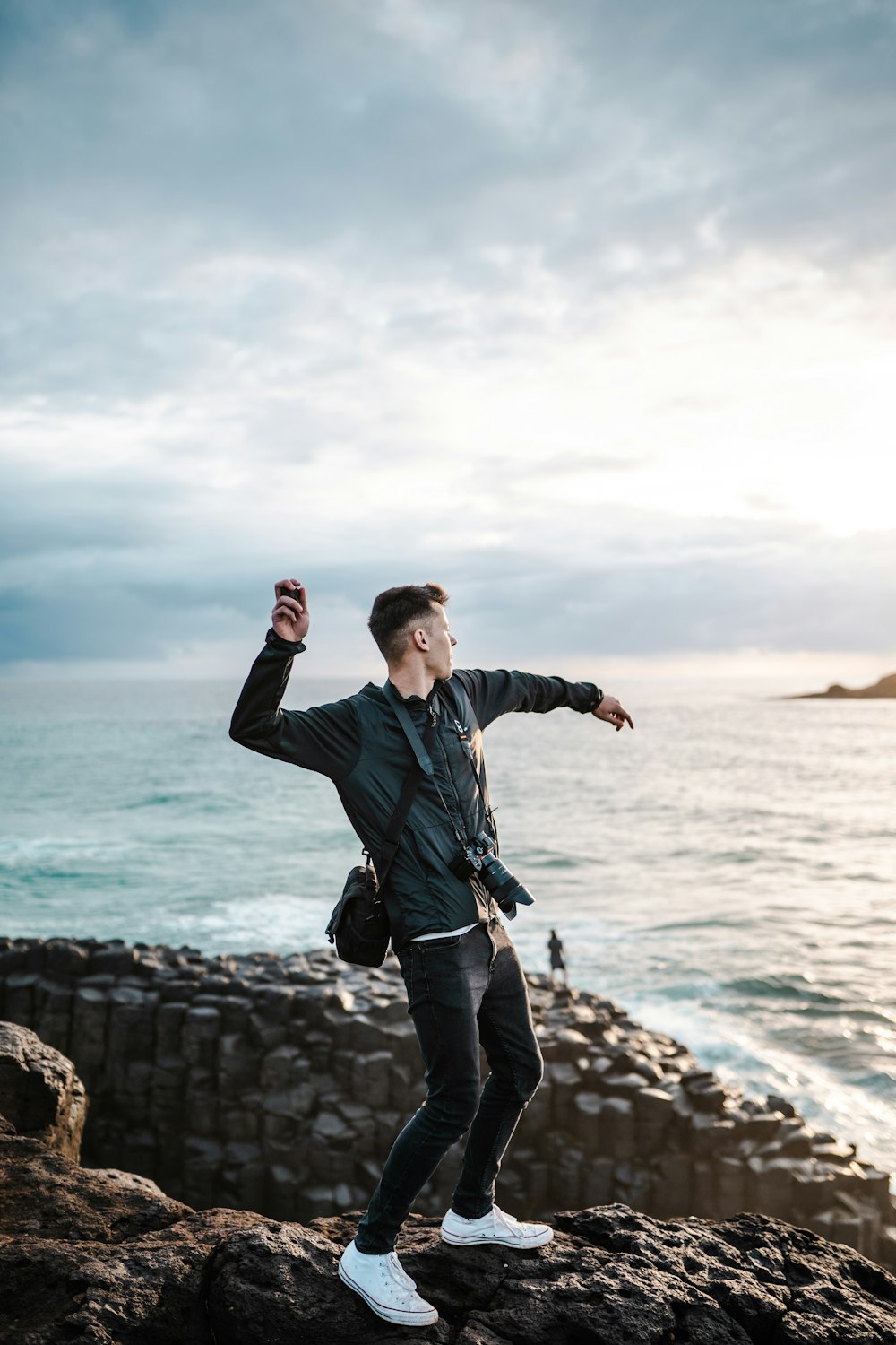 man in blue jacket and black pants standing on rocky shore during daytime