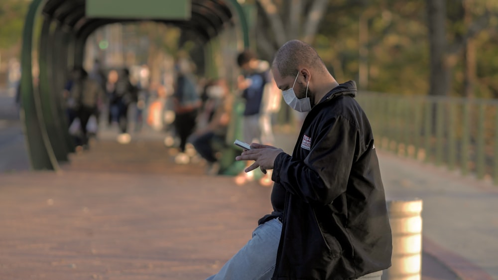 man in black jacket and blue denim jeans sitting on brown wooden bench