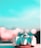 A close-up of a toy race car is positioned on a flat surface with a blurred background. The toy has a sleek, aerodynamic design with a predominantly white body and red accents. The sky above is bright and clear, with a pronounced turquoise hue that enhances the toy's vibrant details.