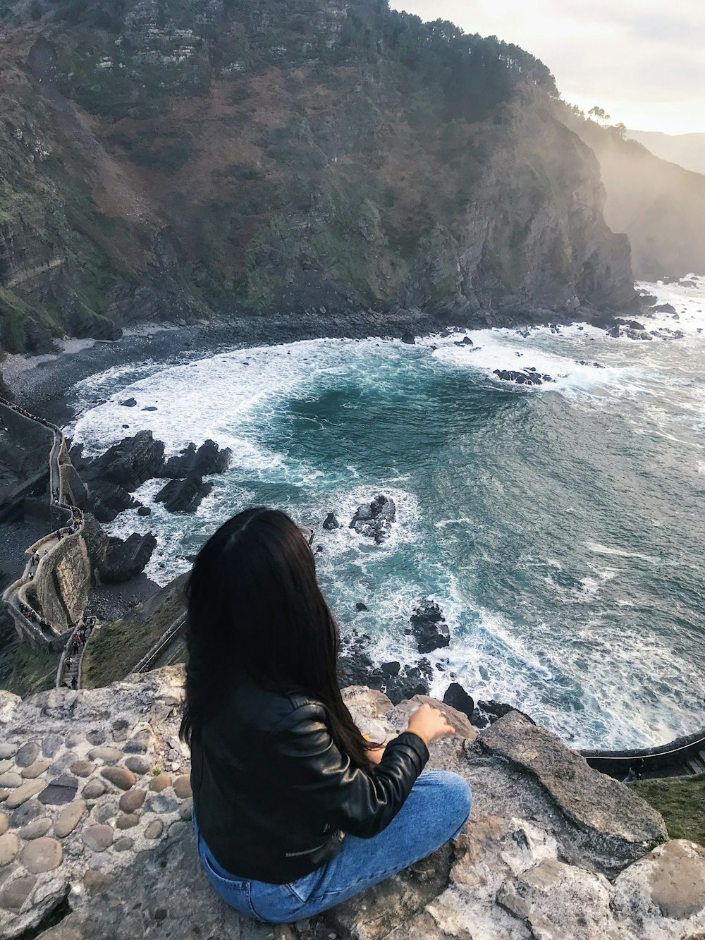 woman in black shirt sitting on rock by the sea during daytime