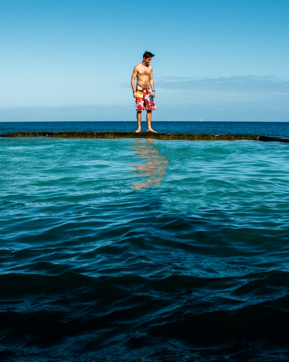 hombre en pantalones cortos azules de pie en la roca en medio del mar durante el día