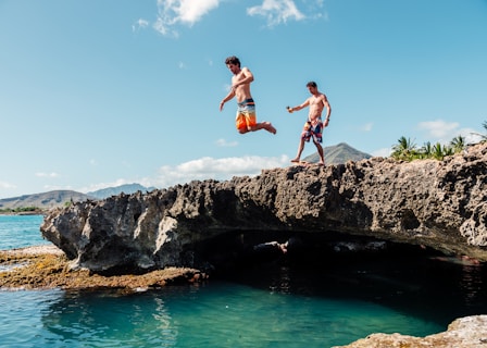 2 boys jumping on rocky mountain during daytime