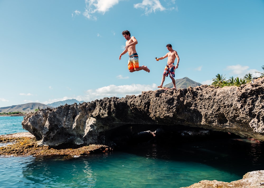 2 boys jumping on rocky mountain during daytime