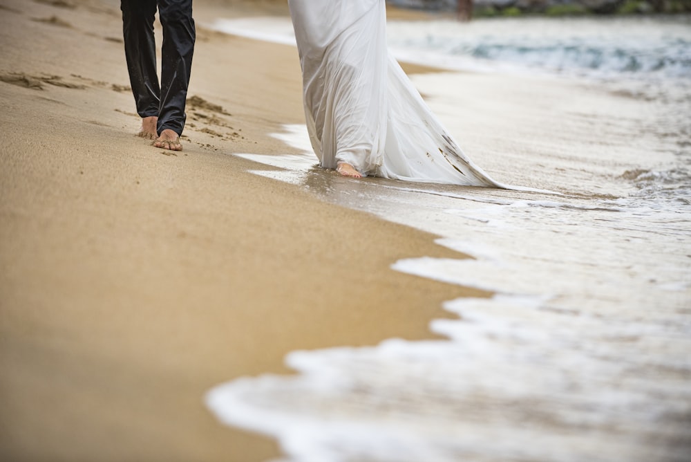 man in white dress shirt and blue denim jeans walking on beach during daytime