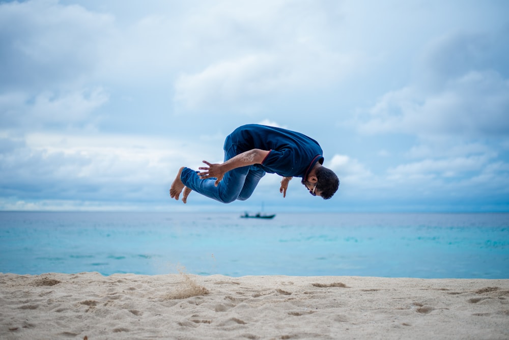 homem de camiseta azul e jeans jeans azuis pulando na praia durante o dia