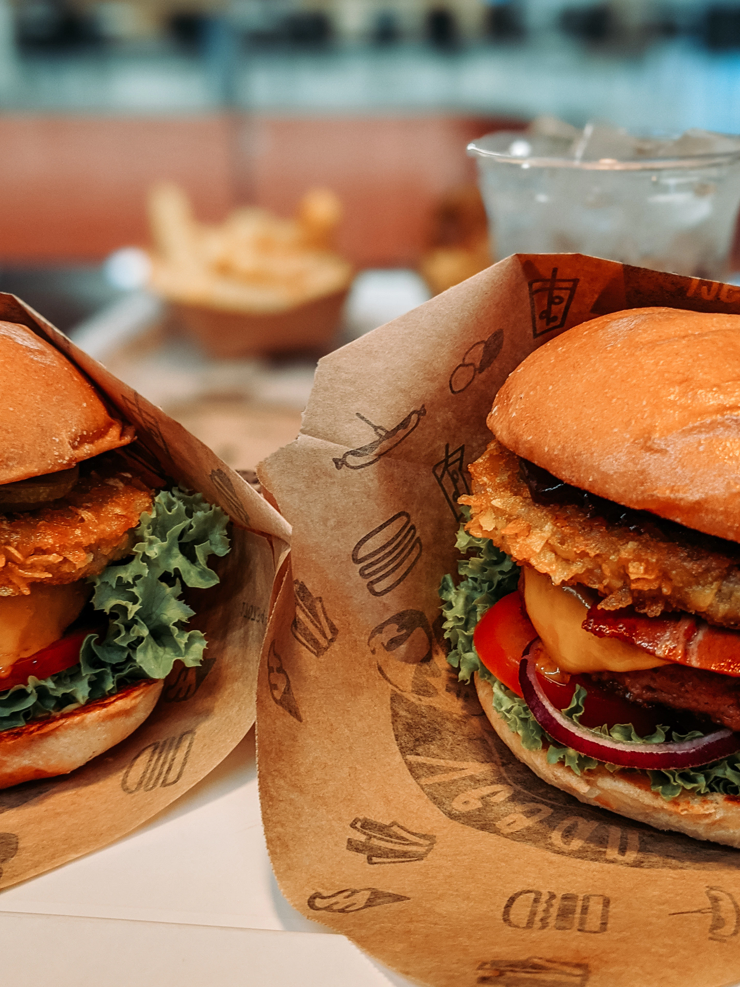 Image décorative représentant deux burgers dans des emballages en papiers, prêts à être dégustés.