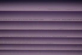 Several purple PVC pipes with black text printed on them. The text includes specifications and a caution that the water is not for drinking.