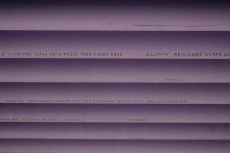 Several purple PVC pipes with black text printed on them. The text includes specifications and a caution that the water is not for drinking.