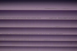 Several purple PVC pipes with black text printed on them. The text includes specifications and a caution that the water is not for drinking.
