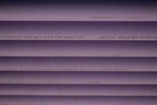 Several purple PVC pipes with black text printed on them. The text includes specifications and a caution that the water is not for drinking.