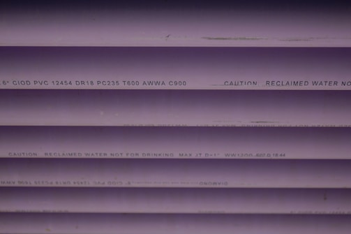 Several purple PVC pipes with black text printed on them. The text includes specifications and a caution that the water is not for drinking.