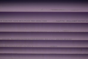 Several purple PVC pipes with black text printed on them. The text includes specifications and a caution that the water is not for drinking.